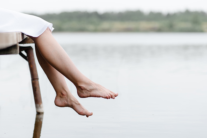 Pair of feet dangling over a bridge by the river.